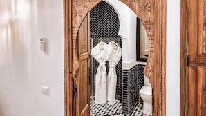 A bathroom with a wooden door, black and white checkered floor, and a white towel rack. - Riad Signature Medina  (Marrakech)