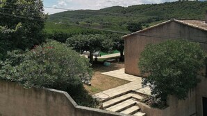 A courtyard with a stone wall, a small building, and a view of a hilly landscape. - Charming, quiet house with patio and pool. Surrounding countryside (Sabran)