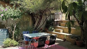 An outdoor patio with a table and chairs, surrounded by potted plants and a wooden staircase. - Charming, quiet house with patio and pool. Surrounding countryside (Sabran)
