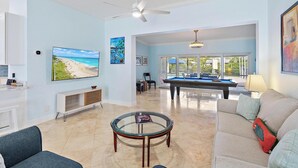 A spacious living room with a pool table, a comfortable sofa, and a television mounted on the wall.