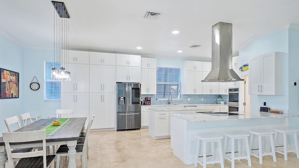 A modern kitchen with white cabinetry, a stainless steel refrigerator, and a central island with bar stools.