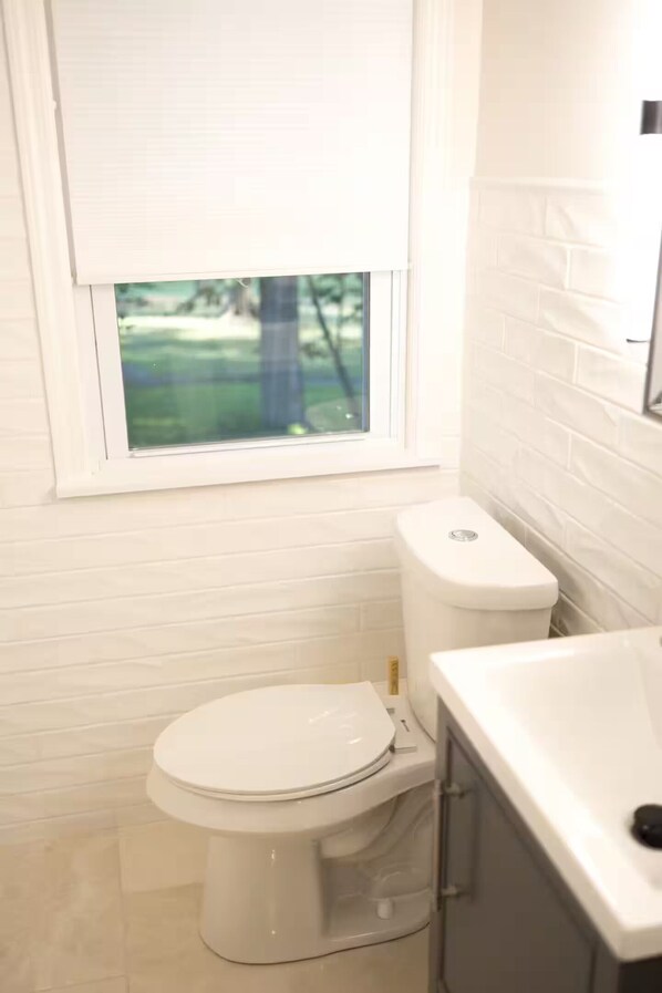 A bathroom with a toilet, a sink, and a window. - The Abigail House (Lyndhurst)