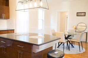 A modern kitchen with a granite countertop, wooden cabinets, and a built-in oven. There is a dining area with a table and chairs. - The Abigail House (Lyndhurst)
