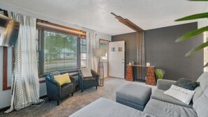 A modern living room with a grey sofa, a blue armchair, and a small table with decorative items. - Welcoming 2-bedroom home with large deck and central location. (Waterloo)