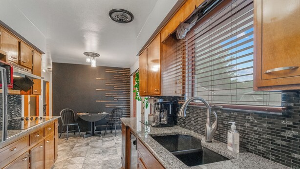A kitchen with wooden cabinets, a granite countertop, a sink, and a dining area with a table and chairs. - Welcoming 2-bedroom home with large deck and central location. (Waterloo)