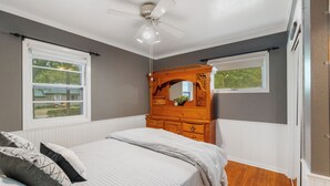 A bedroom with a bed, a wooden dresser, a ceiling fan, and two windows. - Welcoming 2-bedroom home with large deck and central location. (Waterloo)