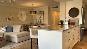 A modern kitchen with a central island, white cabinetry, and a dining area with a sofa and chairs.