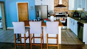 Una cocina con una isla de madera, armarios blancos y un refrigerador de acero inoxidable, además de un microondas.