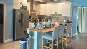 Una cocina con vigas de madera, una isla central con sillas, un refrigerador y un cubo de basura.