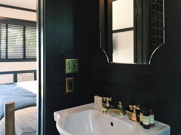 Ein Badezimmer mit einem weißen Waschbecken, einem Spiegel und einem Fenster mit Jalousien.