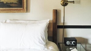 Una habitación de hotel con una cama, una mesita de noche con lámpara y un cuadro en la pared.