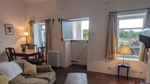 A cozy living room with a sofa, a table, and a window with curtains. - Charming 2-bedroom Cottage near Skibbereen with stove and views. (Skibbereen)