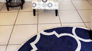 Ein Zimmer mit einem gemusterten Sessel, einem kleinen runden Tisch, zwei gerahmten Bildern an der Wand und einem blauen Teppich auf dem Boden.