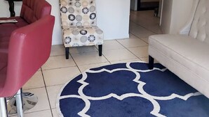 Ein Wohnzimmer mit einem roten Sessel, einem gemusterten Sessel, einem weißen Sofa und einem blauen Teppich.