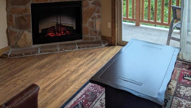 Una sala de estar con chimenea de piedra, un televisor de pantalla plana montado encima y un ventilador de techo.