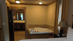 Habitación de hotel con una cama grande, bañera, ventilador de techo y baño con espejo y lavabo.