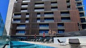 Un hôtel moderne doté d’une piscine sur le toit, avec une eau d’un bleu limpide, des chaises longues et une façade contemporaine agrémentée de lambris en bois verticaux.