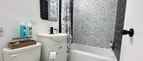 A bathroom with a toilet, sink, and bathtub. There are two bottles of liquid soap on the sink counter.