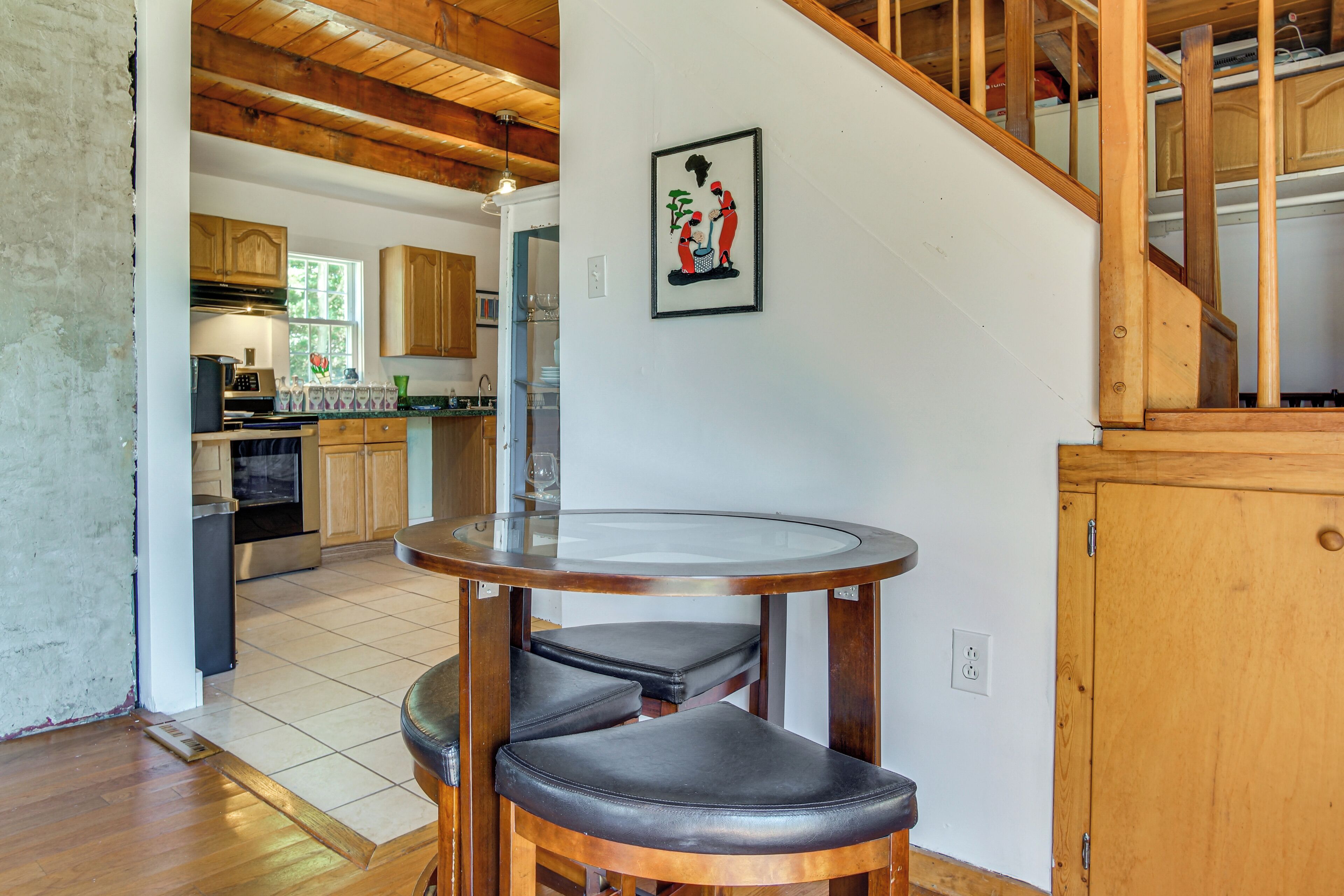 A kitchen with wooden cabinets, a round table with a glass top, and a staircase.