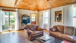 A spacious living room with wooden ceilings and large windows, featuring two leather sofas and a coffee table. - < 1 Mi to Beaches: Home w/ Deck in Oak Bluffs (Oak Bluffs)