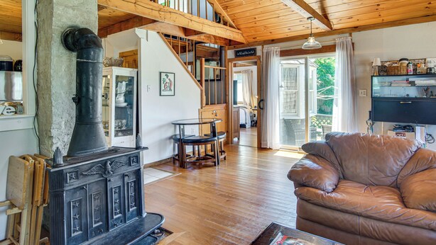A cozy living room with a wooden ceiling, a stone fireplace, a leather sofa, and a dining area with a table and chairs. - < 1 Mi to Beaches: Home w/ Deck in Oak Bluffs (Oak Bluffs)