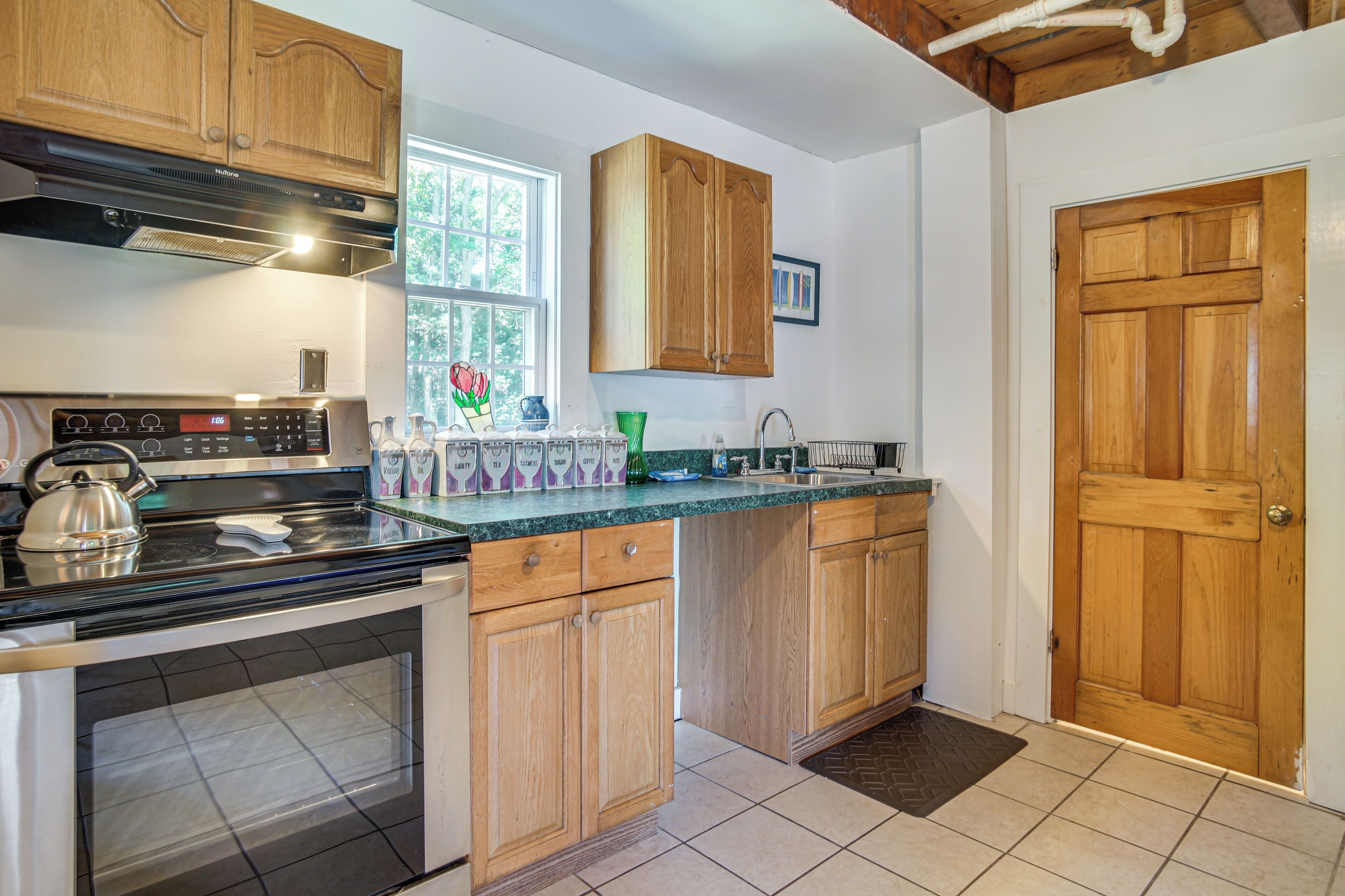 A kitchen with wooden cabinets, a stainless steel stove, and a window with a view of trees.