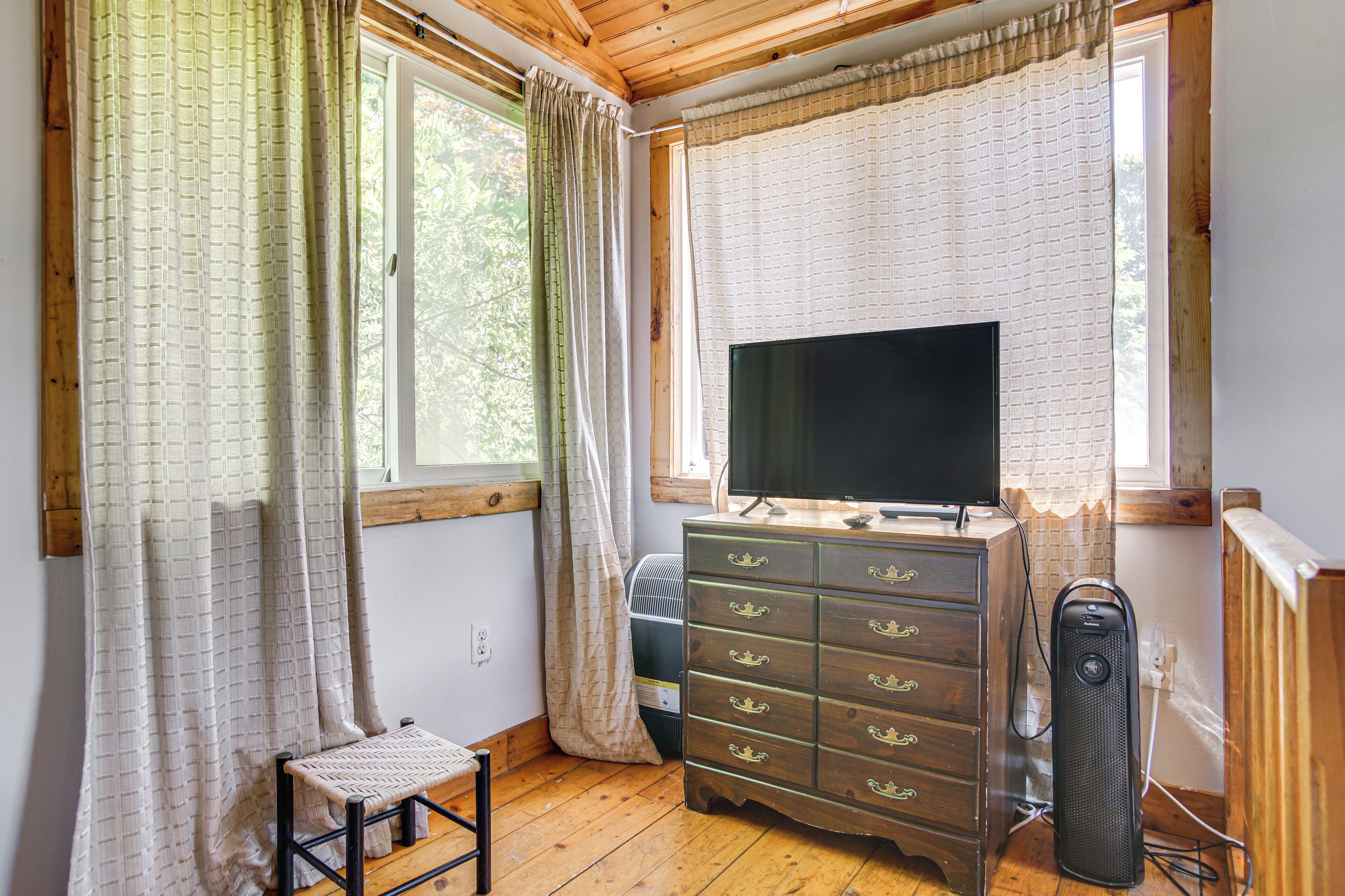 A room with a wooden floor, a TV on a dresser, a chair, and a radiator.