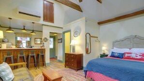 A cozy room with a bed, a sofa, a dining area with chairs, and a kitchen in the background.