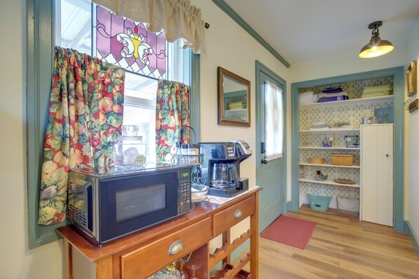 Una cocina con un microondas sobre una encimera de madera, una cafetera y una ventana con cortinas florales.