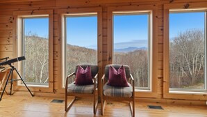 A cabin with large windows, two plaid chairs with purple cushions, and a telescope on the floor.