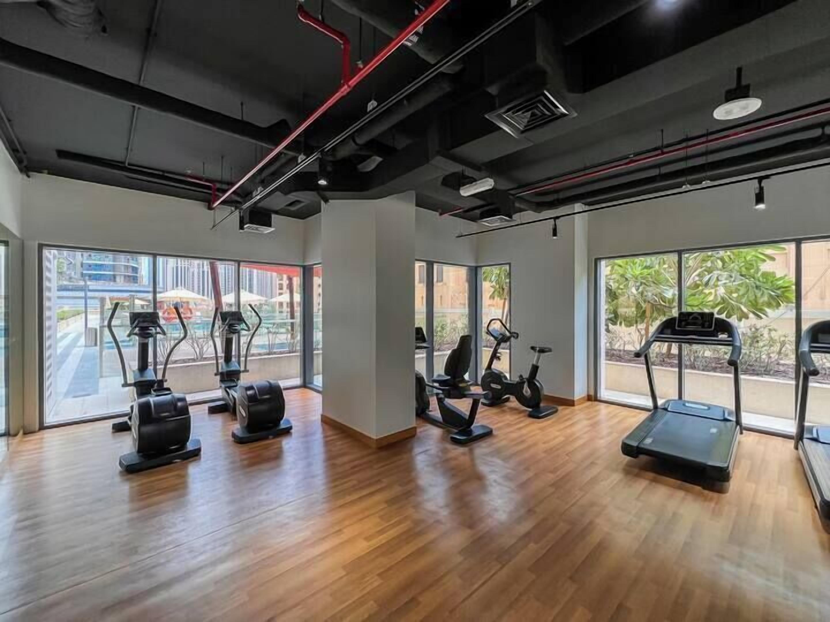 Ein modernes Fitnessstudio mit verschiedenen Trainingsgeräten, großen Fenstern und Holzboden.