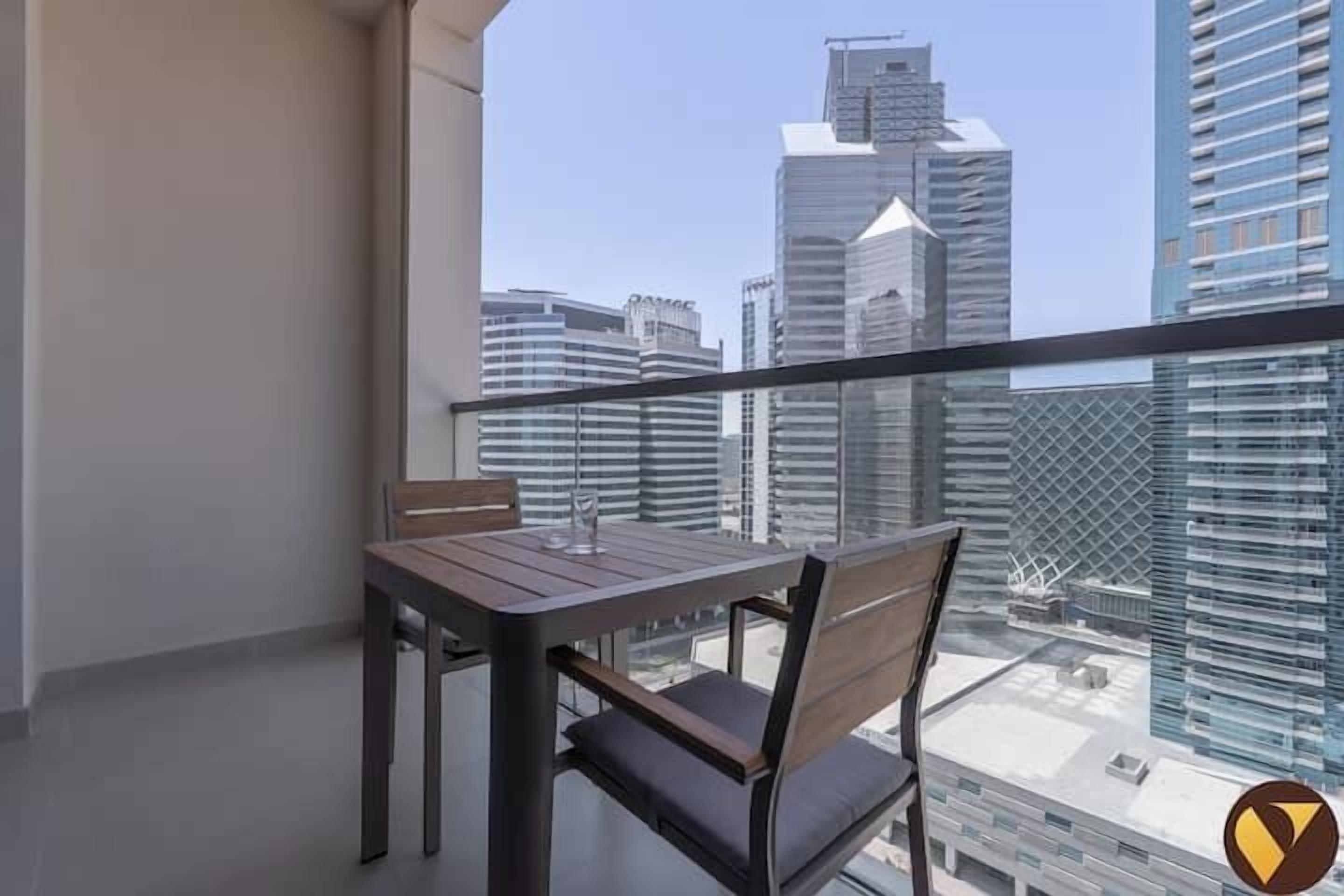 A balcony with a table and chairs, overlooking a cityscape with modern buildings.
