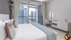 A modern hotel room with a large bed, a desk, and a view of the cityscape through floor-to-ceiling windows.