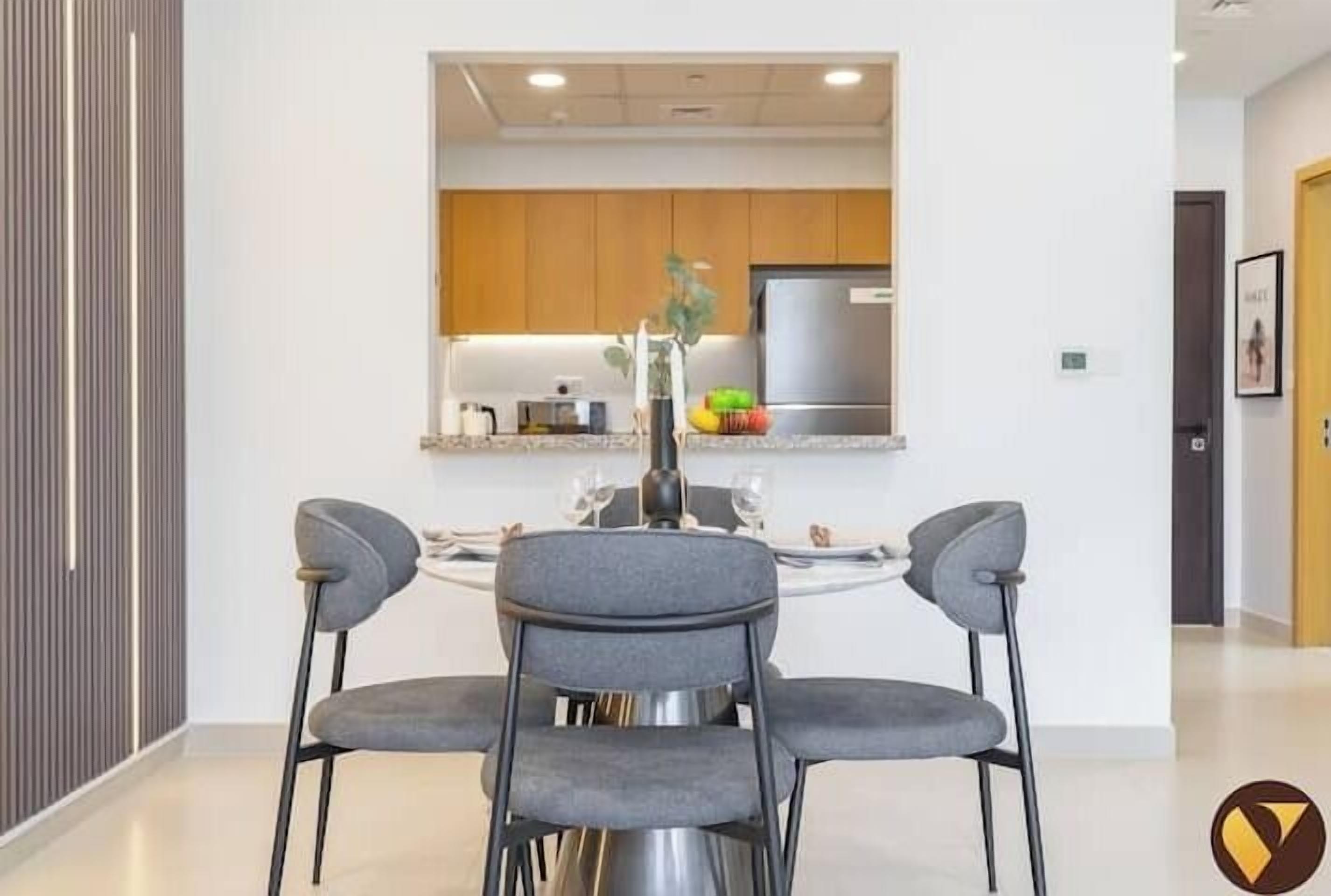 Eine moderne Küche mit Holzausstattung, einem Edelstahlkühlschrank und einer Essecke mit zwei grauen Stühlen und einem runden Tisch.