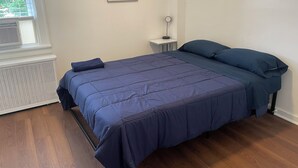 Un dormitorio con cama, mesita de noche, lámpara y ventana con persianas.