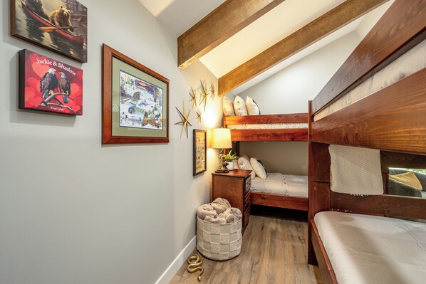 Una habitación acogedora con una cama litera, un escritorio pequeño con una lámpara y cuadros en la pared.