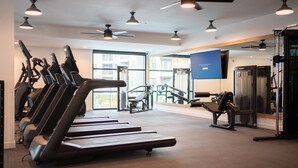 Ein Fitnessstudio mit Laufbändern, Kraftgeräten und Deckenventilatoren.