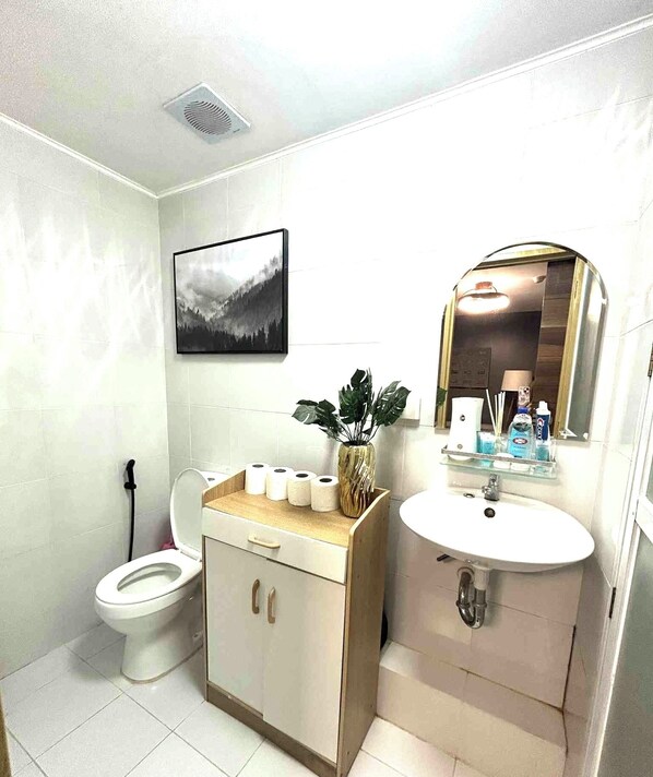 Un baño con inodoro, lavamanos, espejo, un cuadro en la pared y una planta en el mostrador.