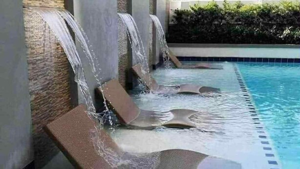 A pool area with multiple water features, including a waterfall and a pool with a tiled edge. - Cozy 2-bedroom condo with AC, fitness room in lovely Iloilo City (Iloilo City)