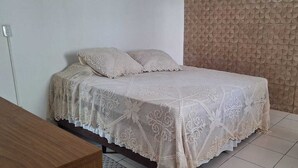 Un llit amb llençols i almoines blancs amb textura, un capçal de fusta i una paret amb un acabat rugós.