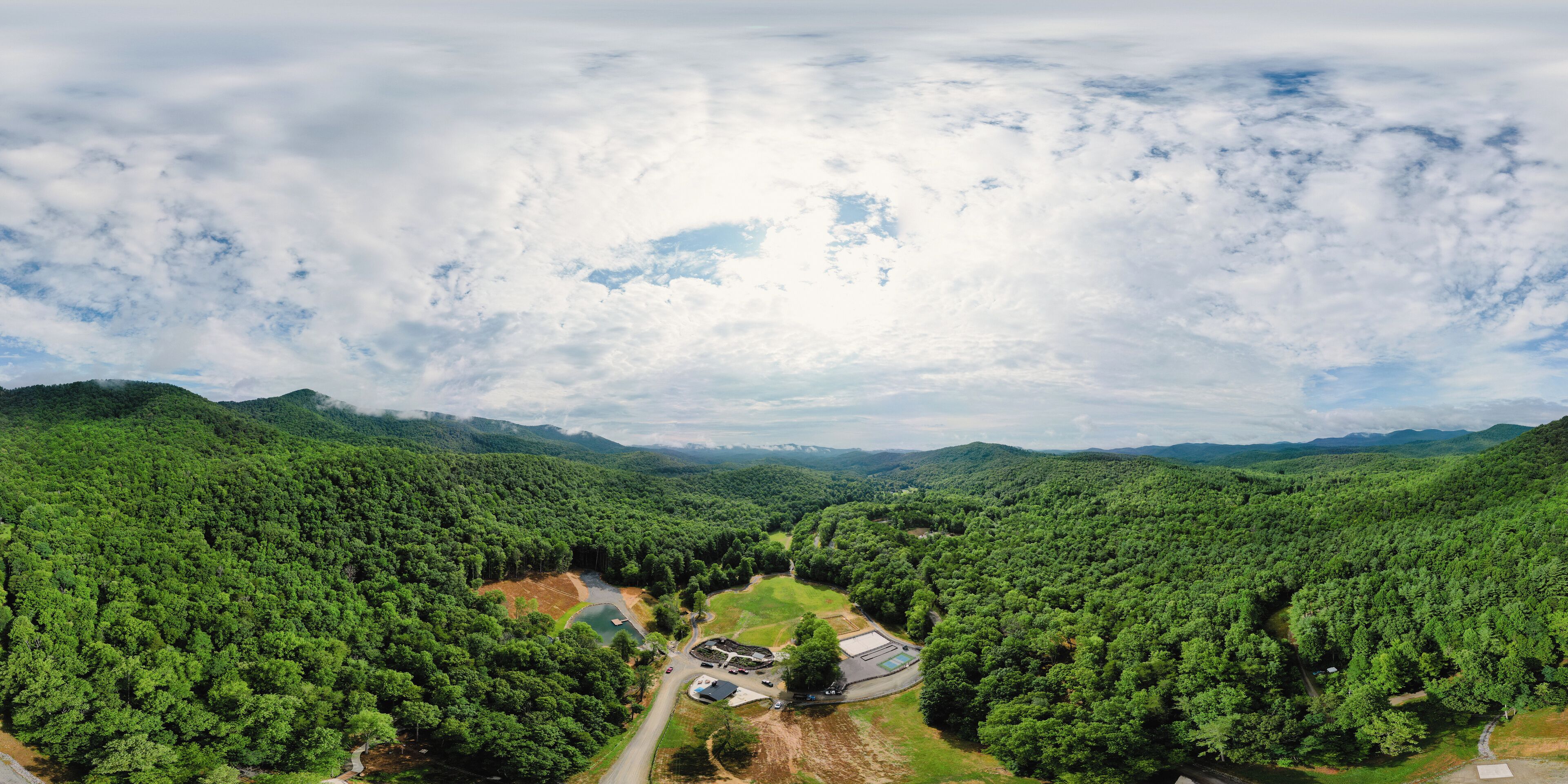 An aerial view of a forested area with a road, a building, and a small lake.