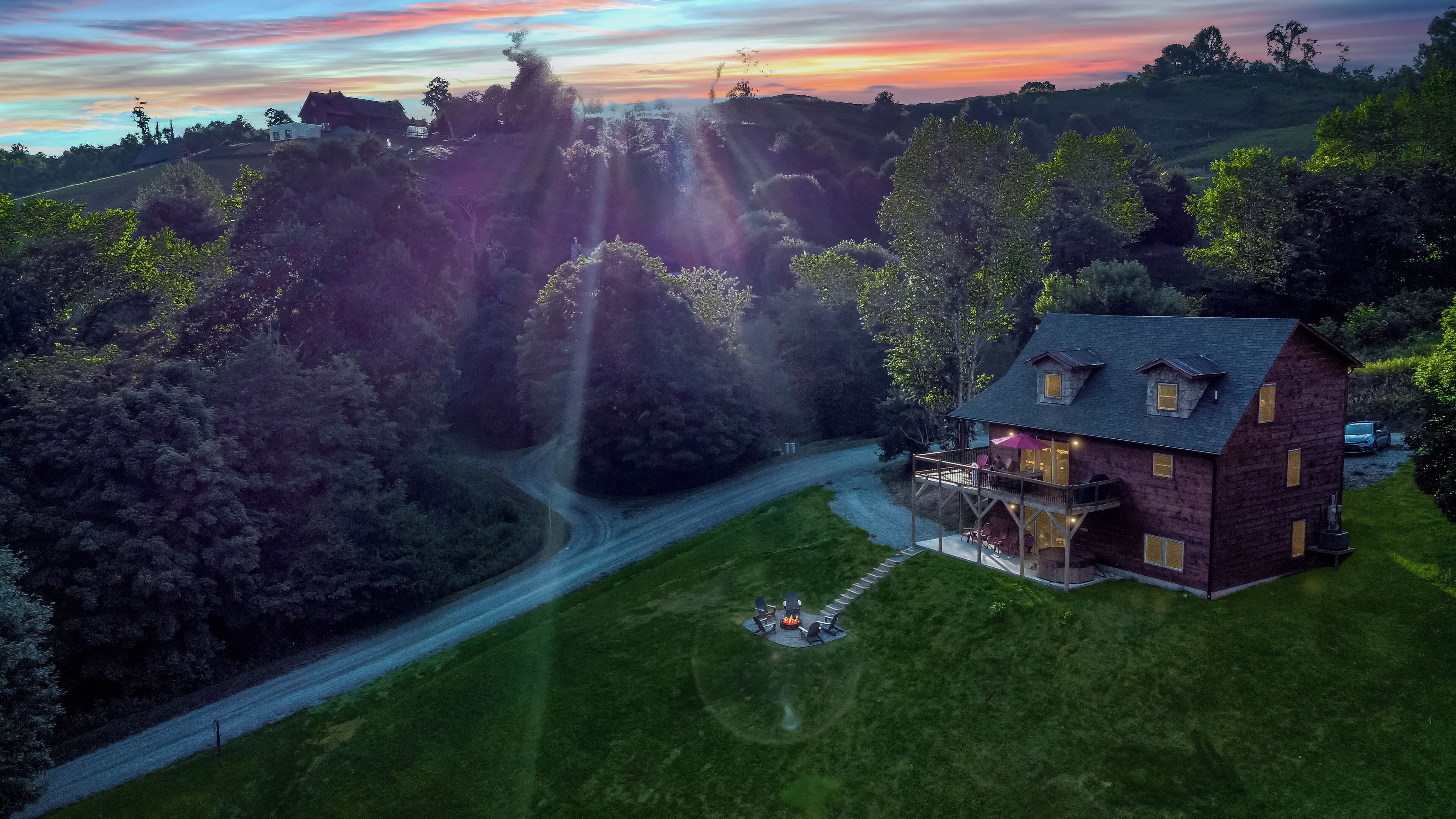 Vue aérienne d’une maison dotée d’une terrasse et d’un espace salon extérieur, entourée d’une végétation luxuriante et bordée d’une route sinueuse.