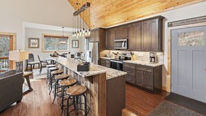 A modern kitchen with wooden ceiling, dark cabinets, and a bar area with stools. - Last Minute Deals! ~Fire Pit, Hot Tub,  on Creek! (Vilas)