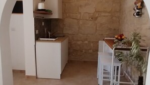 A compact kitchen with a stone wall, white cabinetry, and a small dining area with a plant.