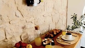 A dining table set with fruits, drinks, and plates, against a stone wall.