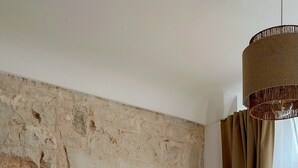 A room with a stone wall, a white sofa with cushions, a small table with a plant, and a hanging light fixture.