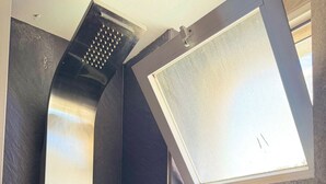 A modern shower with a handheld showerhead and a control panel, adjacent to a window with a view.