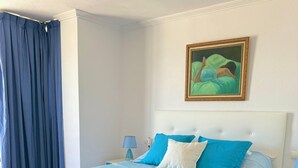 A neatly made bed with blue bedding and matching towels, a white headboard, and a painting on the wall.