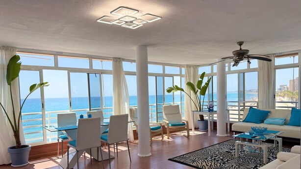 A spacious living area with large windows offering a view of the sea, a ceiling fan, and a modern light fixture.