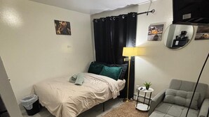 Una habitación pequeña con cama, sofá, una mesita y una lámpara.